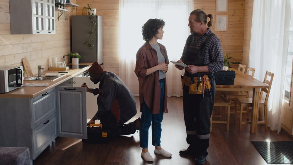 Woman speaking with plumber in kitchen during plumbing repair